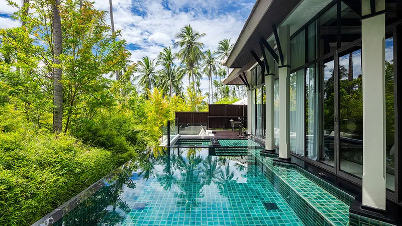 Infinity pool reflecting sky, surrounded by lush greenery at Banyan Tree Samui Wellbeing sanctuary pool villa.